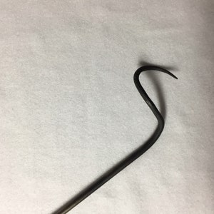 May include: A dark, curved metal hook with a pointed end. The hook has a long, straight handle that bends into a curved shape. The metal has a slightly textured appearance.