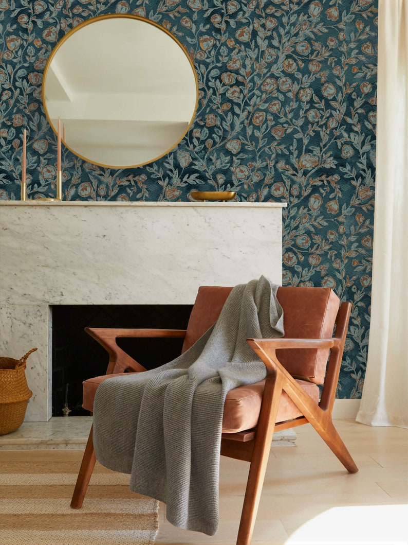May include: A brown leather armchair with a grey knitted throw blanket. The chair is in front of a fireplace with a white marble mantel and a round gold mirror hanging above it. The wall behind the chair is covered in teal wallpaper with a floral pattern.