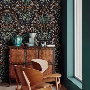 May include: Two wooden chairs with a unique design, featuring a curved back and a wide seat. The chairs are positioned in front of a dark wood cabinet with intricate carvings. The background features a dark teal wall with a wallpaper pattern of stylized trees and flowers in shades of green, orange, and white.