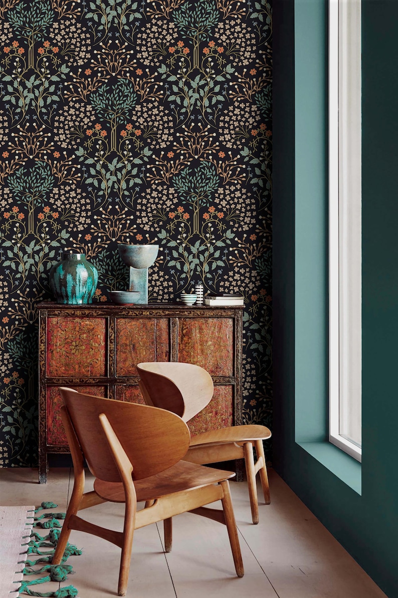 May include: Two wooden chairs with a unique design, featuring a curved back and a wide seat. The chairs are positioned in front of a dark wood cabinet with intricate carvings. The background features a dark teal wall with a wallpaper pattern of stylized trees and flowers in shades of green, orange, and white.