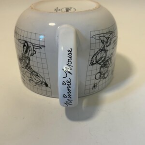 Puede incluir: Taza de cer&aacute;mica blanca con bocetos negros de personajes de dibujos animados sobre un fondo de cuadr&iacute;cula. El asa est&aacute; inscrita con "Minnie Mouse" en cursiva, con dos peque&ntilde;os corazones. Un dise&ntilde;o cl&aacute;sico para los fans.