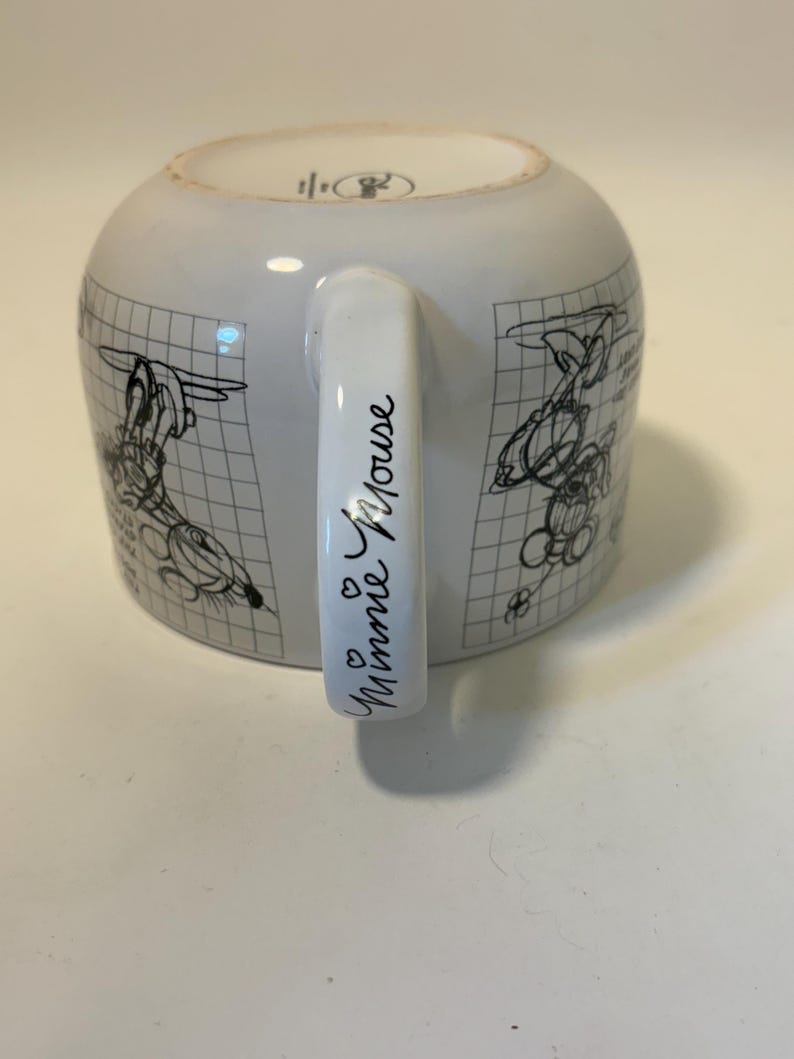 Puede incluir: Taza de cer&aacute;mica blanca con bocetos negros de personajes de dibujos animados sobre un fondo de cuadr&iacute;cula. El asa est&aacute; inscrita con "Minnie Mouse" en cursiva, con dos peque&ntilde;os corazones. Un dise&ntilde;o cl&aacute;sico para los fans.