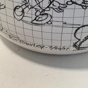 Puede incluir: Una taza de cer&aacute;mica blanca con una ilustraci&oacute;n de dibujos animados en blanco y negro de un personaje. La taza tiene un patr&oacute;n de cuadr&iacute;cula y el texto "Don Towsley eq - 7/20/37" est&aacute; impreso en la parte inferior.