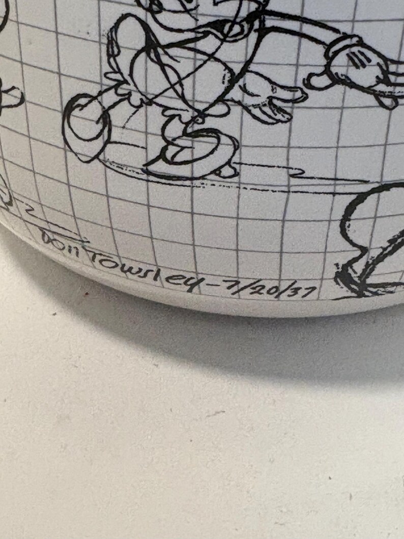 Puede incluir: Una taza de cer&aacute;mica blanca con una ilustraci&oacute;n de dibujos animados en blanco y negro de un personaje. La taza tiene un patr&oacute;n de cuadr&iacute;cula y el texto "Don Towsley eq - 7/20/37" est&aacute; impreso en la parte inferior.