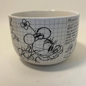 Puede incluir: Cuenco de cer&aacute;mica blanco con un boceto en blanco y negro de Minnie Mouse y texto. El cuenco tiene un patr&oacute;n de cuadr&iacute;cula y presenta un dibujo de Minnie Mouse con una flor y el texto "Minnie is of the basic const..."