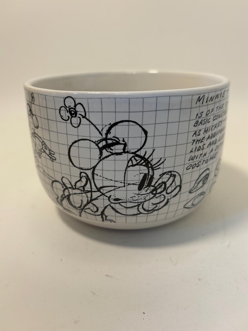 Puede incluir: Cuenco de cer&aacute;mica blanco con un boceto en blanco y negro de Minnie Mouse y texto. El cuenco tiene un patr&oacute;n de cuadr&iacute;cula y presenta un dibujo de Minnie Mouse con una flor y el texto "Minnie is of the basic const..."