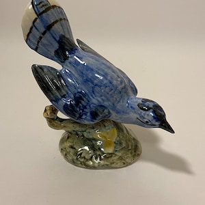 May include: A blue and white ceramic figurine of a blue jay perched on a branch. The bird has a detailed design and is painted in shades of blue, white, and black.