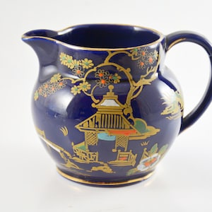 May include: A cobalt blue ceramic milk jug with a gold and multi-coloured floral and pagoda design.