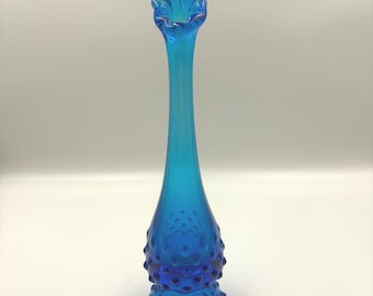 Op de afbeelding: Een hoge, slanke vaas van felblauw glas met een textuur van noppen op de bolvormige basis. De vaas heeft een lange, gladde hals die overgaat in een geplooide, geschulpte opening aan de bovenkant, wat zorgt voor een doorschijnende afwerking.