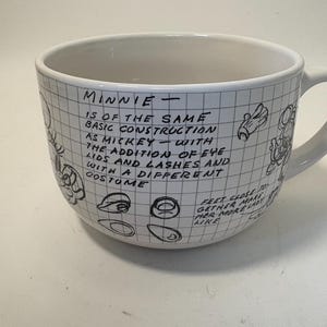 Puede incluir: Taza de cer&aacute;mica blanca con un patr&oacute;n de cuadr&iacute;cula y texto y bocetos escritos a mano en negro. El texto dice "MINNIE" y describe la construcci&oacute;n de Minnie Mouse. Tambi&eacute;n hay bocetos de las caracter&iacute;sticas de Minnie.