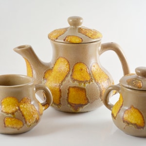 May include: A ceramic tea set with a brown and yellow glaze. The set includes a teapot, creamer, and sugar bowl.