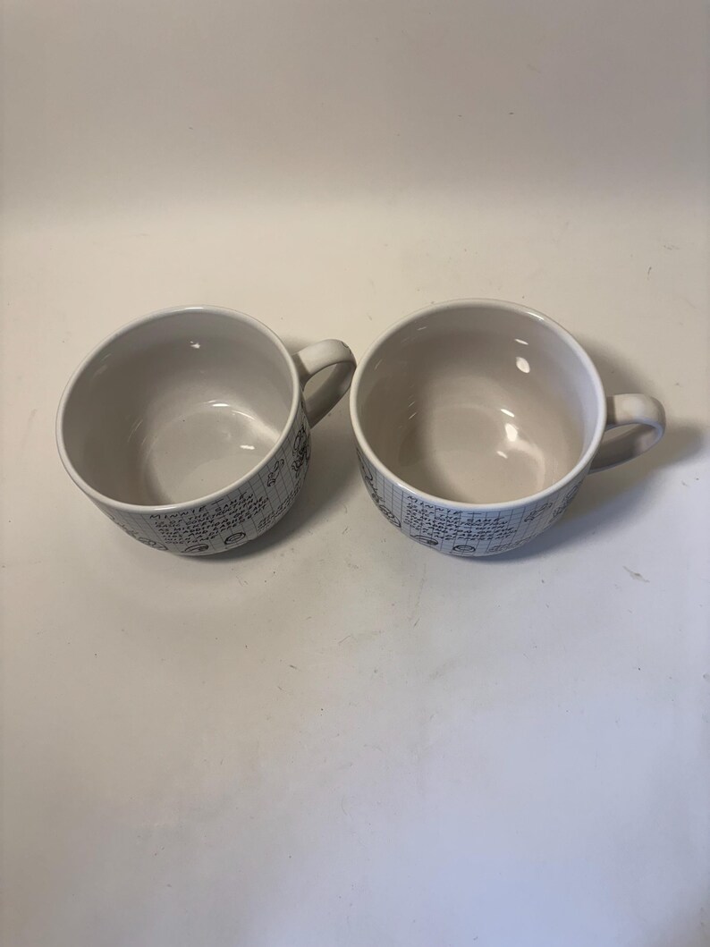 Puede incluir: Dos tazas de sopa de cer&aacute;mica blanca con asas. Las tazas tienen forma redondeada y un interior de color claro. El exterior de cada taza presenta un patr&oacute;n repetido de texto manuscrito y peque&ntilde;as ilustraciones en color azul oscuro.