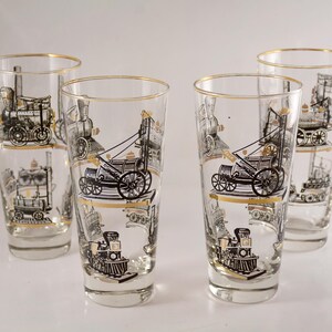May include: Set of four clear glass tumblers with gold rims. Each tumbler features a black and white illustration of a vintage steam locomotive.