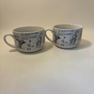 Puede incluir: Dos tazas de cer&aacute;mica blanca con asas. Cada taza presenta una ilustraci&oacute;n de dibujos animados en blanco y negro y un texto manuscrito que dice "TRY FOR DAINTY HAND POSITIONS. THE SHIRT IS SLIGHTLY STARCHED AND USUALLY STICKS UP."