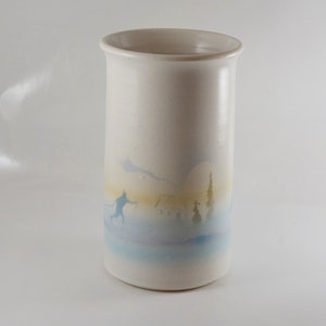 May include: White ceramic vase with a winter scene painted on the side. The scene includes a skier, a house, and trees. The vase is approximately 18 cm tall.