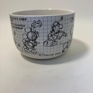 Puede incluir: Cuenco de cer&aacute;mica blanca con dibujos lineales negros de Mickey y Minnie Mouse sobre un fondo de cuadr&iacute;cula. El cuenco tiene texto y est&aacute; firmado por Don Townley-Wagner. Una pieza encantadora para los fans de Disney.