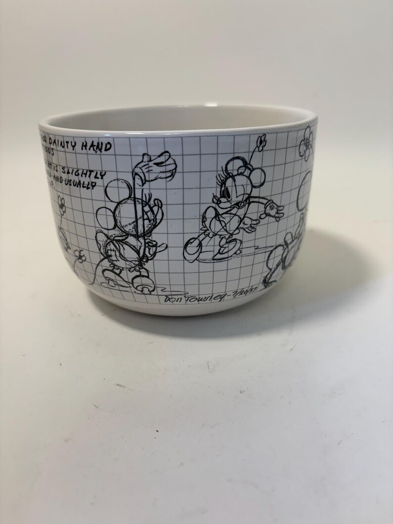 Puede incluir: Cuenco de cer&aacute;mica blanca con dibujos lineales negros de Mickey y Minnie Mouse sobre un fondo de cuadr&iacute;cula. El cuenco tiene texto y est&aacute; firmado por Don Townley-Wagner. Una pieza encantadora para los fans de Disney.