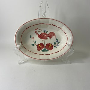 May include: White ceramic bowl with a red rooster design and green leaves. The bowl has a scalloped edge and a red and white trim.
