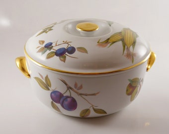 May include: White porcelain casserole dish with a gold rim and lid. The dish is decorated with a floral pattern of plums, corn, and leaves.