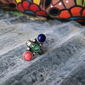 May include: A silver ring with three stones: a green turquoise, a blue lapis lazuli, and a pink coral.