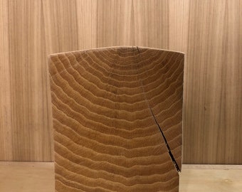 May include: A solid wood block with a natural wood finish. The block has a rounded top and a rough, textured surface. The wood grain is visible and shows the rings of the tree.