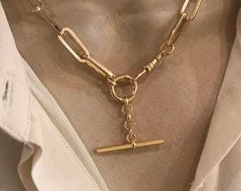 May include: A gold chain necklace with a t-bar clasp. The chain is made of large, rectangular links.