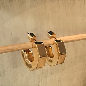 May include: A pair of gold-toned hexagonal hoop earrings. The earrings are simple and modern in design.