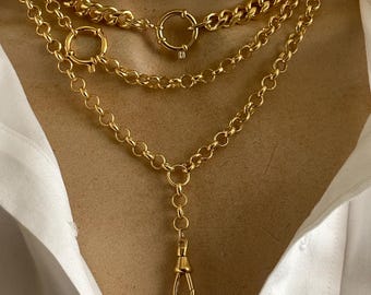 May include: Three gold necklaces of varying styles are displayed. The top necklace is a thick curb chain, the middle is a delicate chain with a large ring clasp, and the bottom has a long drop with a lobster clasp. The necklaces are worn over a white shirt.