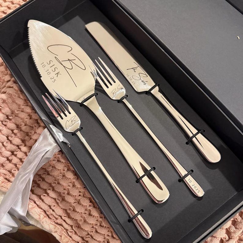Personalized 4-piece champagne gold wedding cake cutting set with custom script monograms and date engraving, presented inside a premium black magnetic gift box. The high-polish stainless steel set is shown against a soft rose textured knit backdrop.