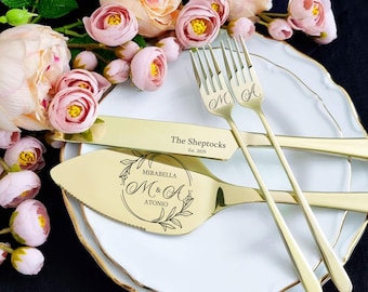 Könnte beinhalten: Goldene Hochzeitstortenmesser und -gabeln mit gravierten Namen und dem Text "The Sheptocks Est. 2025" und "Mirabella M&A Antonio" in einem Kreis mit floralen Designs.
