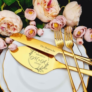 Personalized 4-piece vibrant gold wedding cake cutting set. Mirror-polished stainless steel server features a botanical wreath with Mirabella and Antonio. Knife engraved with The Sheptocks est. 2025. Displayed on a gold-rimmed plate with peach roses.