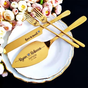 Personalized 4-piece vibrant gold wedding cake cutting set for Ryan and Rebecca Rapson, 07-17-2026. Knife features 'Love is sweet' and blue crystal hearts. Set is displayed on stacked white gold-rimmed plates with romantic peach roses.