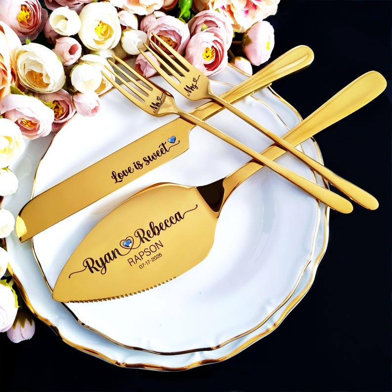 Personalized 4-piece vibrant gold wedding cake cutting set for Ryan and Rebecca Rapson, 07-17-2026. Knife features 'Love is sweet' and blue crystal hearts. Set is displayed on stacked white gold-rimmed plates with romantic peach roses.