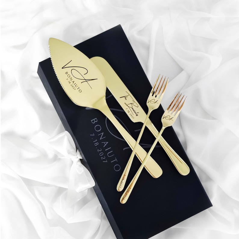 Personalized champagne gold wedding cake knife, server, and forks. Sleek mirror-polished stainless steel, laser engraving. Placed on custom black magnetic gift box over white satin. Minimalist newlywed gift and heirloom keepsake.