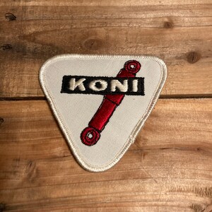 May include: White triangular patch with a red and black shock absorber graphic and the word "KONI" in black lettering.
