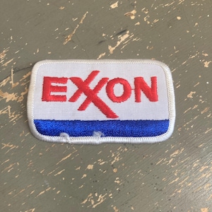 May include: Rectangular patch with the word "EXXON" in red block letters on a white background. The bottom of the patch has a blue stripe. The patch has a white border.