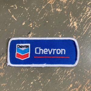 May include: A rectangular blue Chevron patch with white trim. The Chevron logo, featuring red, white, and blue chevrons, is on the left. The word "Chevron" is embroidered in white with a red line beneath it.