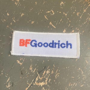 May include: A white rectangular patch with the text "BFGoodrich" in red and blue. The patch is on a distressed gray surface.