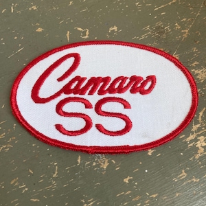 May include: Oval-shaped patch with the word "Camaro" in red script above the letters "SS". The patch has a white background with a red border.