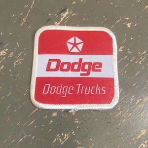 May include: A square patch with a white border and a red and white design. The top section is red with a white star in the center. The word "Dodge" is in red, and "Dodge Trucks" is below it.