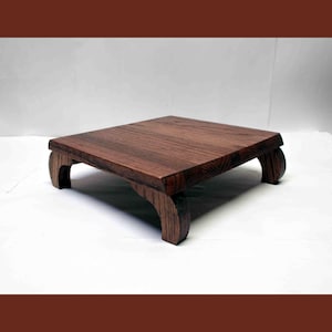 May include: A small, square wooden table with a dark brown finish. The table has a flat top and curved legs. The table is approximately 12 inches long, 12 inches wide, and 6 inches tall. The table is made of wood.