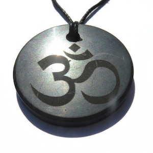 Könnte beinhalten: Ein schwarzer Steinanhänger mit silbernem Schimmer und einem gravierten Om-Symbol. Der Anhänger ist an einer schwarzen Schnur.