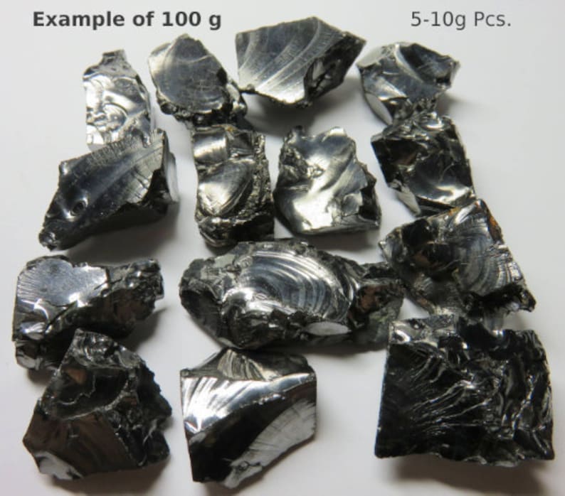 K&ouml;nnte beinhalten: Nahaufnahme einer Sammlung von 100 Gramm schwarzen, metallischen, unregelm&auml;&szlig;ig geformten Steinen. Der Bildtext lautet "Beispiel von 100 g" und "5-10g Stk."