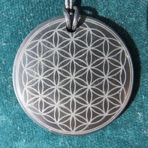 Könnte beinhalten: Ein schwarzer Steinanhänger mit einem silberfarbenen Lebensblume-Design. Der Anhänger ist an einer schwarzen Schnur befestigt.