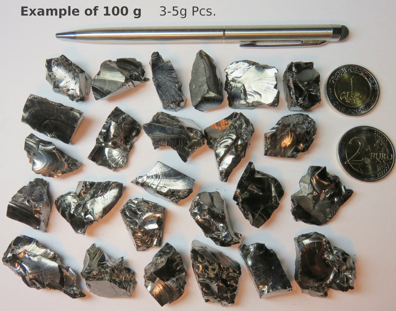 K&ouml;nnte beinhalten: Beispiel f&uuml;r 100 Gramm schwarzer, metallischer, unregelm&auml;&szlig;ig geformter St&uuml;cke. Die St&uuml;cke sind zwischen 3 und 5 Gramm schwer. Ein Stift und zwei Euro-M&uuml;nzen dienen als Gr&ouml;&szlig;envergleich.