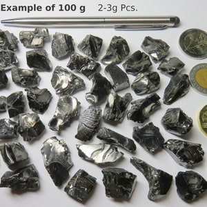 K&ouml;nnte beinhalten: Beispiel f&uuml;r 100 Gramm schwarzes Obsidian, mit 2-3 Gramm gro&szlig;en St&uuml;cken. Das Obsidian wird neben einem Stift, einer 2-Euro-M&uuml;nze, einer 1-Euro-M&uuml;nze, einer 200-Forint-M&uuml;nze und einer 2-Euro-M&uuml;nze gezeigt.