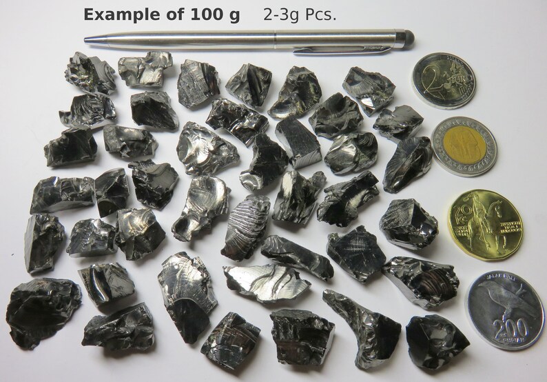 K&ouml;nnte beinhalten: Beispiel f&uuml;r 100 Gramm schwarzes Obsidian, mit 2-3 Gramm gro&szlig;en St&uuml;cken. Das Obsidian wird neben einem Stift, einer 2-Euro-M&uuml;nze, einer 1-Euro-M&uuml;nze, einer 200-Forint-M&uuml;nze und einer 2-Euro-M&uuml;nze gezeigt.