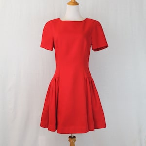 May include: A red short-sleeved dress with a fitted bodice and a flared skirt. The dress is on a wooden mannequin.