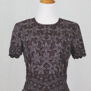 May include: A brown beaded top with a floral design. The top has short sleeves and a scalloped hem.