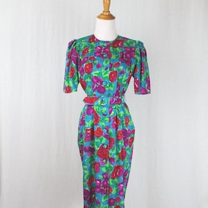 Puede incluir: Un vestido azul con estampado floral con flores rojas y moradas. El vestido tiene un frente abotonado y un cintur&oacute;n.